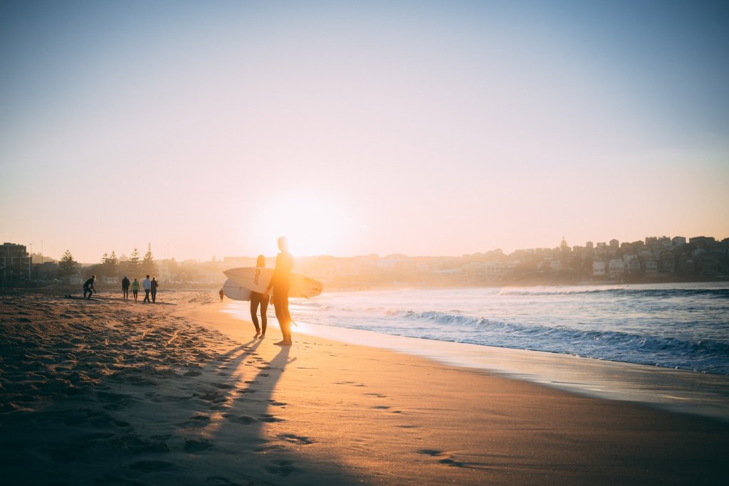 Surfers walking along the shore with golden light on the beach