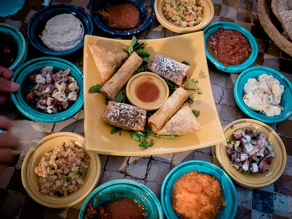 assortment of Moroccan dishes in small bowls with a bigger plate of food in the center