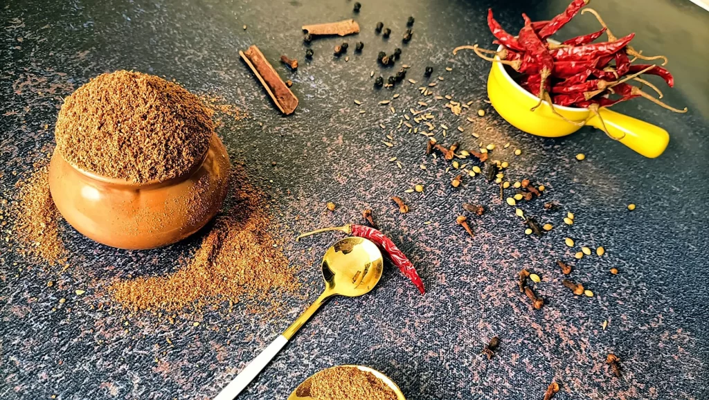 bowls of spices and loose spices on a black surface
