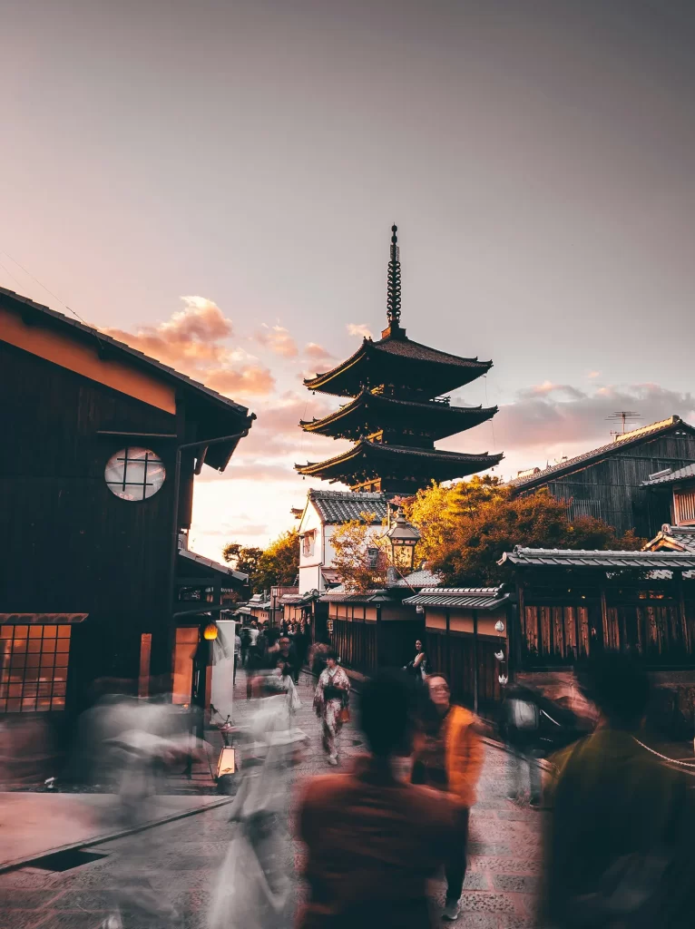 Blurry people walking down a street with a Japanese temple in the background