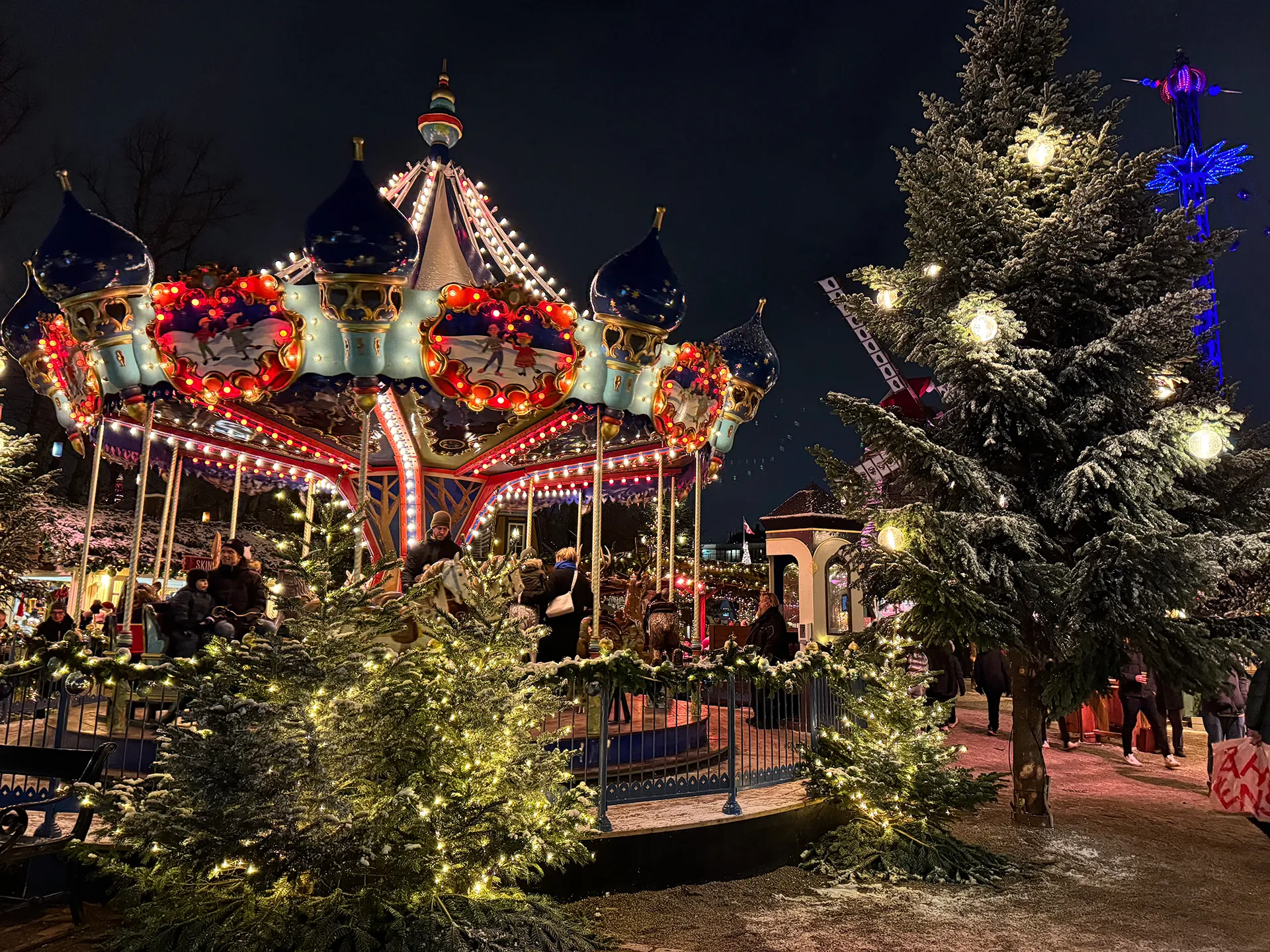 Carousel at Tivoli Gardens in Denmark during the holiday season. The carousel and trees are decked out with Christmas lights.