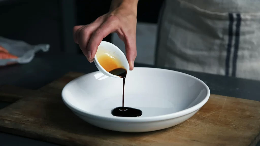 Hand pouring balsamic vinegar into a white bowl