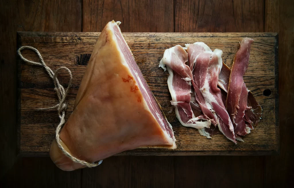 Prosciutto di Parma ham whole and sliced on a wooden cutting board